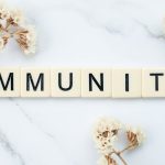 Elegantly arranged scrabble tiles spelling 'immunity' on a marble background with white flowers.