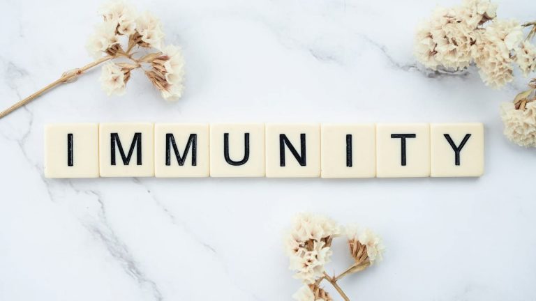 Elegantly arranged scrabble tiles spelling 'immunity' on a marble background with white flowers.